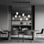 Lampa wisząca Astral 9-punktowa w kolorze czarnym i multikolorowym z szklanymi kloszami o owalnym kształcie, zawieszona na cienkich linkach. Ujęcie frontalne, w nowoczesnym wnętrzu z okrągłym stołem i krzesłami w odcieniach szarości.