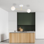 Lampa sufitowa Magnum 2-punktowa w białej i złotej kolorystyce, z okrągłymi kloszami, zamontowana na suficie w nowoczesnej kuchni. Widok z dołu, lampa z dwiema kulami umieszczonymi na złotych ramionach. Tło w odcieniach bieli i zieleni.