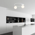 Lampa sufitowa Sopra 2-punktowa w kolorze białym z opalowymi kloszami, zamontowana na białym suficie. W tle nowoczesna kuchnia z białymi meblami i czarnymi półkami. Klosze w kształcie kul, zawieszone na okrągłej, metalowej ramie.