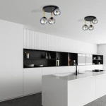 Lampa sufitowa Dolce 3-punktowa w kolorze czarnym, złotym i grafitowym. Składa się z trzech szklanych kul na złotych prętach, zamontowana na czarnej podstawie. Widoczna w nowoczesnej kuchni z białymi meblami i ciemnym tłem.