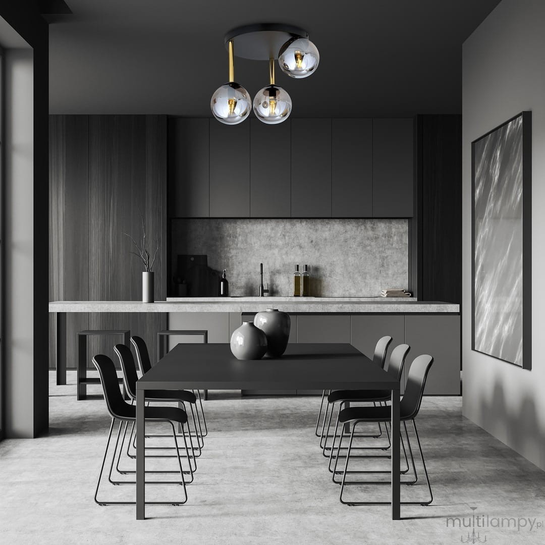 Lampa sufitowa Dolce 3-punktowa w kolorze czarnym, złotym i grafitowym, z trzema szklanymi kloszami. Zawieszona pod sufitem w nowoczesnej kuchni, nad czarnym stołem z dekoracyjnymi naczyniami. Kąt ujęcia frontalny, z widokiem na otoczenie.