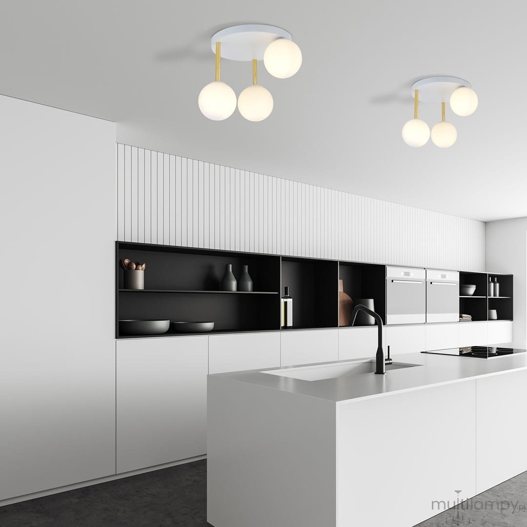 Lampa sufitowa Dolce 3-punktowa w kolorze białym i złotym z opalowymi kloszami. Zawieszona na trzech złotych prętach, umieszczona na białym, okrągłym stelażu. Widoczna w nowoczesnej kuchni z białymi meblami i czarnymi akcentami.