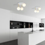 Lampa sufitowa Dolce 3-punktowa w kolorze białym i złotym z opalowymi kloszami. Zawieszona na trzech złotych prętach, umieszczona na białym, okrągłym stelażu. Widoczna w nowoczesnej kuchni z białymi meblami i czarnymi akcentami.