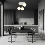 Lampa sufitowa Dolce 3-punktowa w kolorze białym i złotym z opalowymi kulami. Zawieszona na trzech złotych prętach, umieszczona w nowoczesnej kuchni z ciemnymi meblami i dużym stołem.