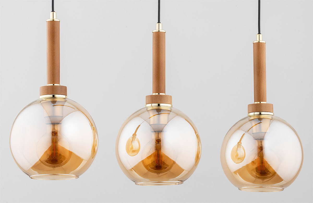 Lampa wisząca Balerina 3-punktowa z przezroczystymi kulami w złotym odcieniu, z drewnianymi uchwytami. Ujęcie frontalne, lampy zwisają na czarnych przewodach, w tle jasnoszare. Widoczne żarówki wewnątrz kul.