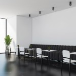 Czarna tuba lampa sufitowa 1-punktowa, zamontowana na białym suficie, w nowoczesnym wnętrzu kawiarni. W tle widoczna kanapa, stoliki oraz rośliny w donicach. Lampa ma cylindryczny kształt, dodając minimalistycznego akcentu do aranżacji.