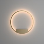 Kinkiet Rim D60 LED w mosiężnym kolorze, w kształcie okręgu, zamontowany na ścianie. Emituje miękkie, ciepłe światło wokół obwodu. Posiada prostą, minimalistyczną formę z płaskim, dyskretnym mocowaniem. Tło w jasnym odcieniu.