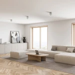 Biała lampa sufitowa Rondoo 1-punktowa, kierunkowa, zamontowana na suficie. Prosty, cylindryczny kształt, minimalistyczny design. W tle nowoczesny salon z jasnymi meblami i dużymi oknami.