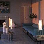 Lampa stołowa Cipresso 1-punktowa w złotym kolorze, z eleganckim abażurem, umieszczona na okrągłym stoliku w nowoczesnym wnętrzu. Widoczny niebieski sofa i dekoracyjne elementy, jak wazon i okrągłe doniczki.