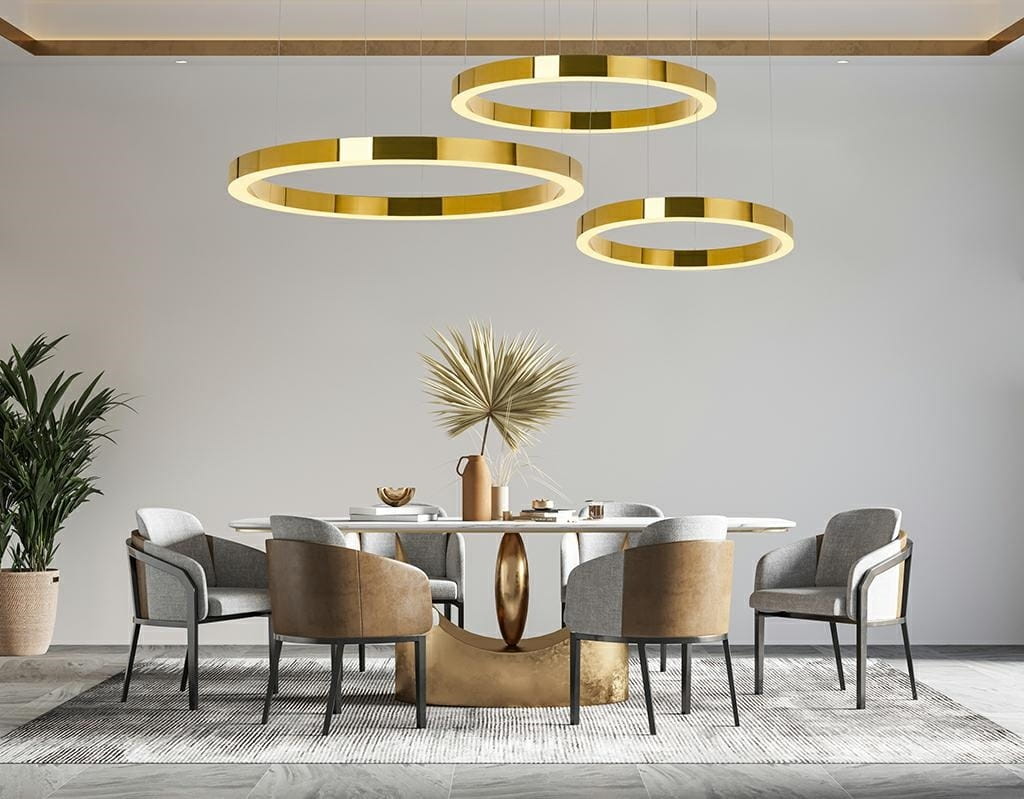 Lampa wisząca Ring Luxury 110 LED w kolorze złotym, składająca się z trzech okrągłych pierścieni, zawieszona nad stołem w nowoczesnej jadalni. Otoczenie z jasnymi krzesłami i roślinami, na tle neutralnej ściany.