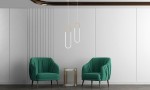 Złota lampa wisząca Puzo S LED, 1-punktowa, w kształcie pętli. Zawieszona w nowoczesnym wnętrzu, nad zielonymi fotelami. Prosta forma, połączenie metalu i szkła, idealna do stylowych aranżacji.
