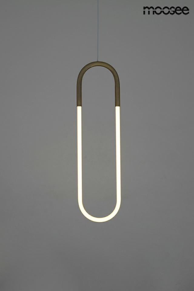 Lampa wisząca Puzo S LED w złotym kolorze, o nowoczesnym, owalnym kształcie. Zawieszona na cienkim przewodzie, emituje miękkie światło. Tło w jednolitym, szarym kolorze podkreśla elegancję lampy.