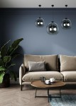 Lampa wisząca Sandra 30, czarna, o okrągłym kształcie, zawieszona na cienkim kablu. W tle widoczny stylowy salon z jasnoniebieską ścianą, brązową sofą i okrągłym stolikiem kawowym. Dodatkowo roślina w doniczce po lewej stronie.