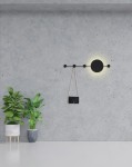 Kinkiet Shadow Hang LED w kolorze czarnym, z okrągłym źródłem światła i wieszakiem na torbę. Zamontowany na szarej ścianie, w towarzystwie roślin doniczkowych. Prosta, nowoczesna forma, idealna do wnętrz.