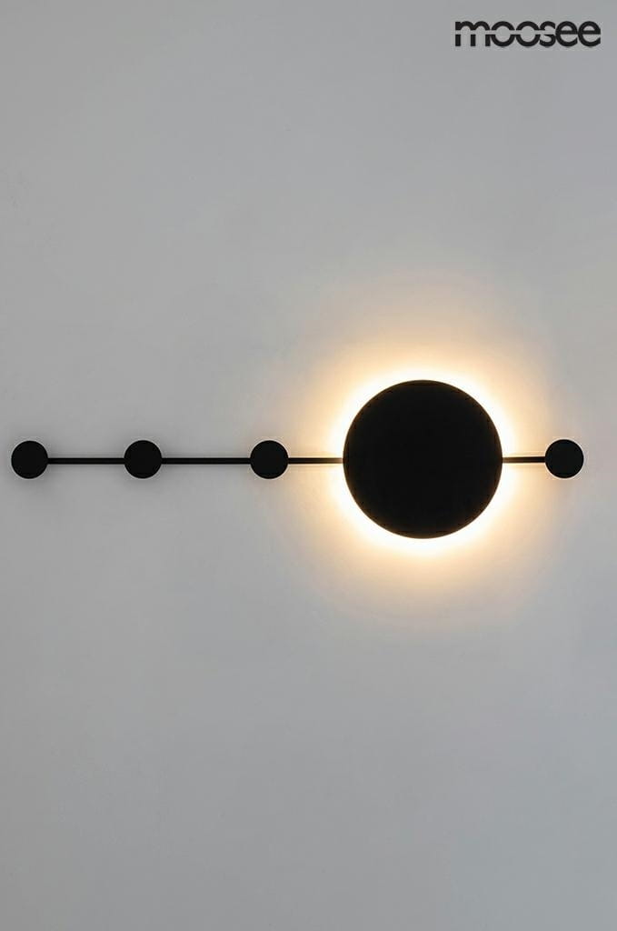 Czarny kinkiet LED Shadow Hang z jednym źródłem światła, umieszczony na ścianie. Okrągła lampa emitująca światło w otoczeniu czterech małych, okrągłych wieszaków. Prosta, nowoczesna forma na jasnym tle.