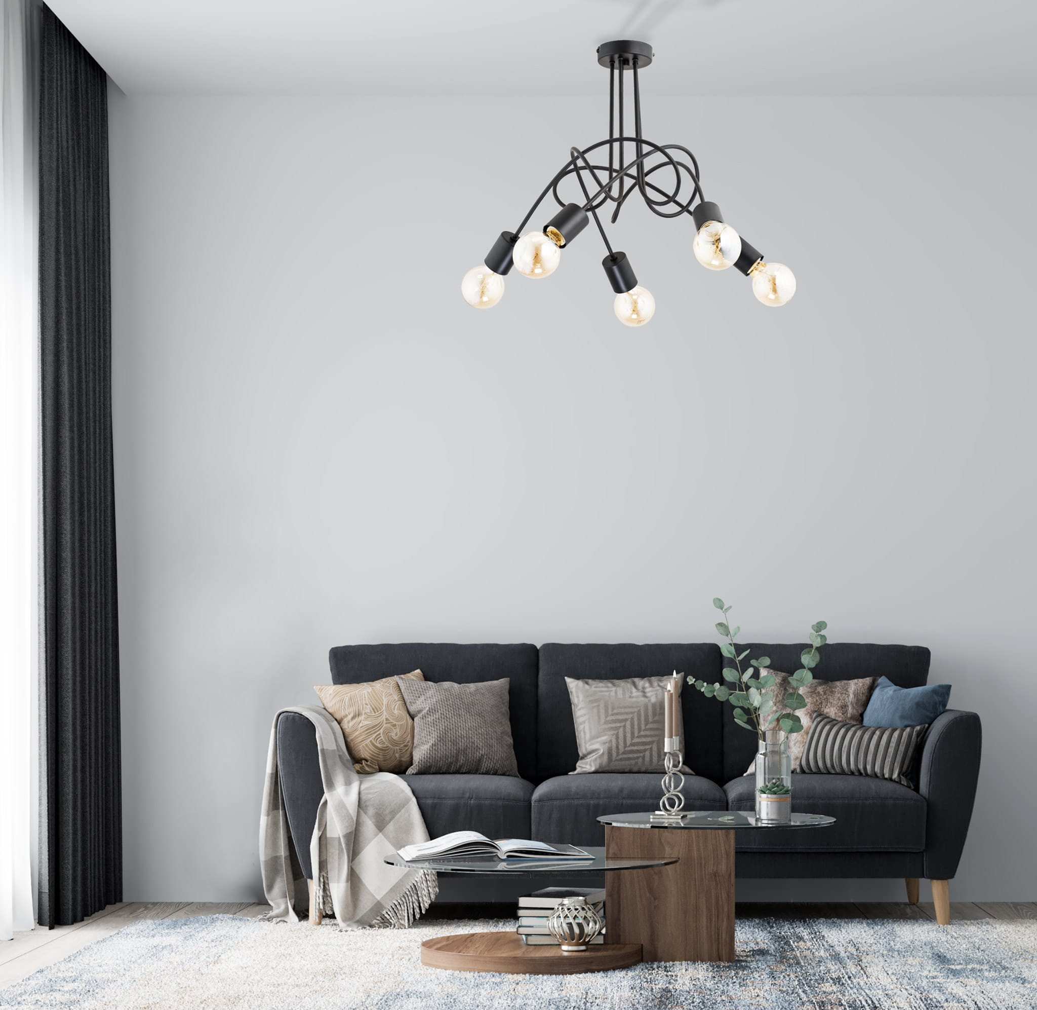Czarna lampa wisząca 5-punktowa Tango z metalowymi ramionami, umieszczona na suficie, z pięcioma przezroczystymi żarówkami. Lampa w nowoczesnym stylu, w tle widoczny ciemnoszary sofa z poduszkami oraz stół kawowy.