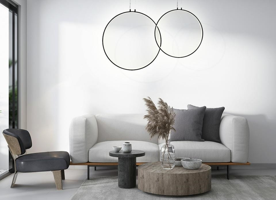 Czarna lampa wisząca Circulo 80 LED z dwoma okrągłymi obręczami, zawieszona nad szarym, prostym stołem w nowoczesnym wnętrzu. W tle widać jasną ścianę i kanapę z poduszkami oraz roślinność za oknem.