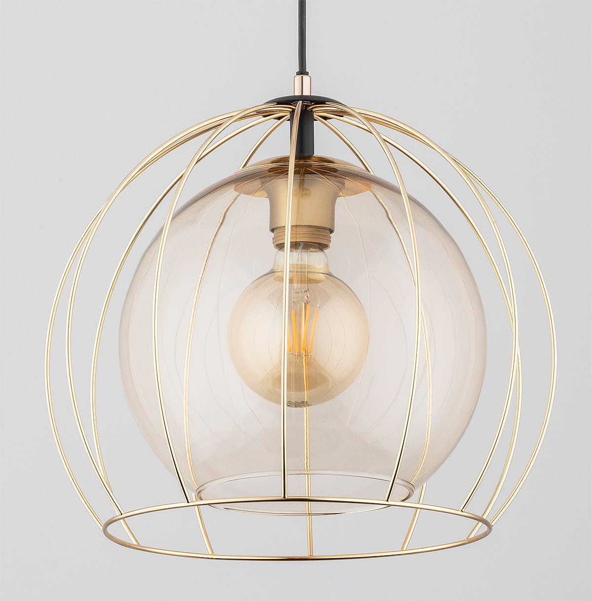 Lampa wisząca Avango 1-punktowa w kolorze czarnym i złotym. Szklany klosz w kształcie kuli osłonięty złotą metalową siatką. Widoczna żarówka w środku. Zawieszona na czarnym przewodzie. Prosta, nowoczesna forma.