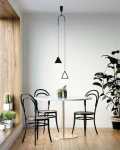 Czarna lampa wisząca Acustica LED 2-punktowa z geometrycznymi kloszami w kształcie stożka i trójkąta, zawieszona w minimalistycznym wnętrzu nad okrągłym stołem, w otoczeniu drewnianej podłogi i roślin.