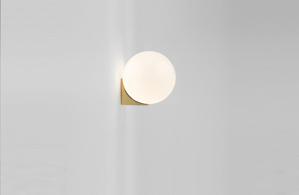 Złoty kinkiet Boll z jedną oprawą, z okrągłym, mlecznym kloszem. Ujęcie frontalne, zamontowany na jasnej ścianie. Prosta, nowoczesna forma z minimalistycznym designem, idealny do różnych aranżacji wnętrz.