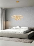 Złota lampa wisząca Liberty Triples LED z trzema punktami świetlnymi, umieszczona nad łóżkiem w sypialni. Lampa ma nowoczesny, okrągły kształt z przeplatanymi elementami, zawieszona na cienkich linkach. Tło o jasnej, gładkiej ścianie i naturalnym świetle.