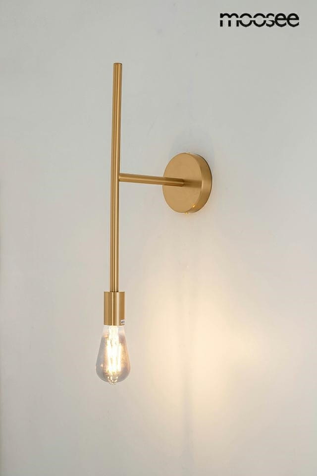 Kinkiet Riva w kolorze złotym, z pojedynczym źródłem światła, prostą, metalową konstrukcją i okrągłą podstawą. Lampa wisi na ścianie, a widoczna żarówka ma kształt kropli. Tło jasne, jednolite.