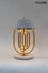 Lampa stołowa Bottega z dwoma punktami świetlnymi, z okrągłą białą kloszem i złotą metalową podstawą. Kształt lampy jest nowoczesny, z dekoracyjnymi metalowymi rurkami, umieszczona na okrągłej białej podstawie. Tło neutralne.