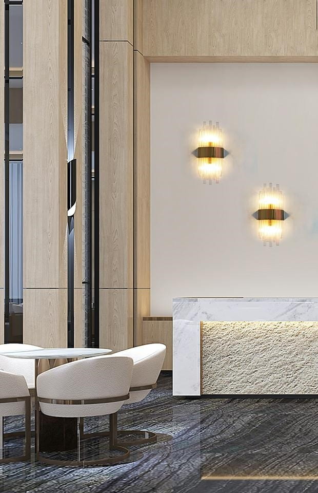 Portofino kinkiet 2-punktowy w kolorze złotym, zamontowany na jasnej ścianie. Oświetlenie emituje ciepłe światło, podkreślając nowoczesny design. W tle widoczne eleganckie krzesła i stół w przestronnej aranżacji wnętrza.