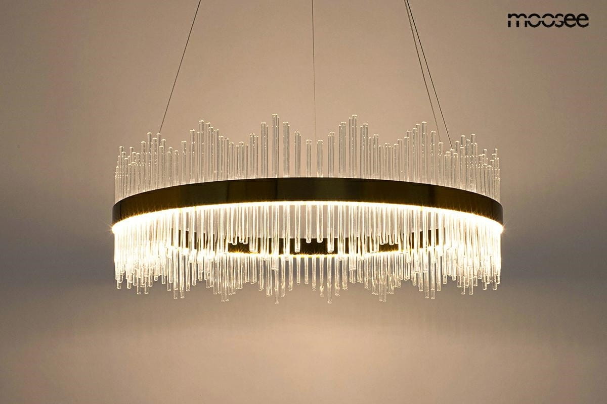 Lampa wisząca Florens 80 LED w kolorze złotym, o okrągłym kształcie, z dekoracyjnymi, przezroczystymi elementami w formie szklanych prętów. Zawieszona na cienkich linkach, emituje ciepłe światło, idealna do nowoczesnych wnętrz.