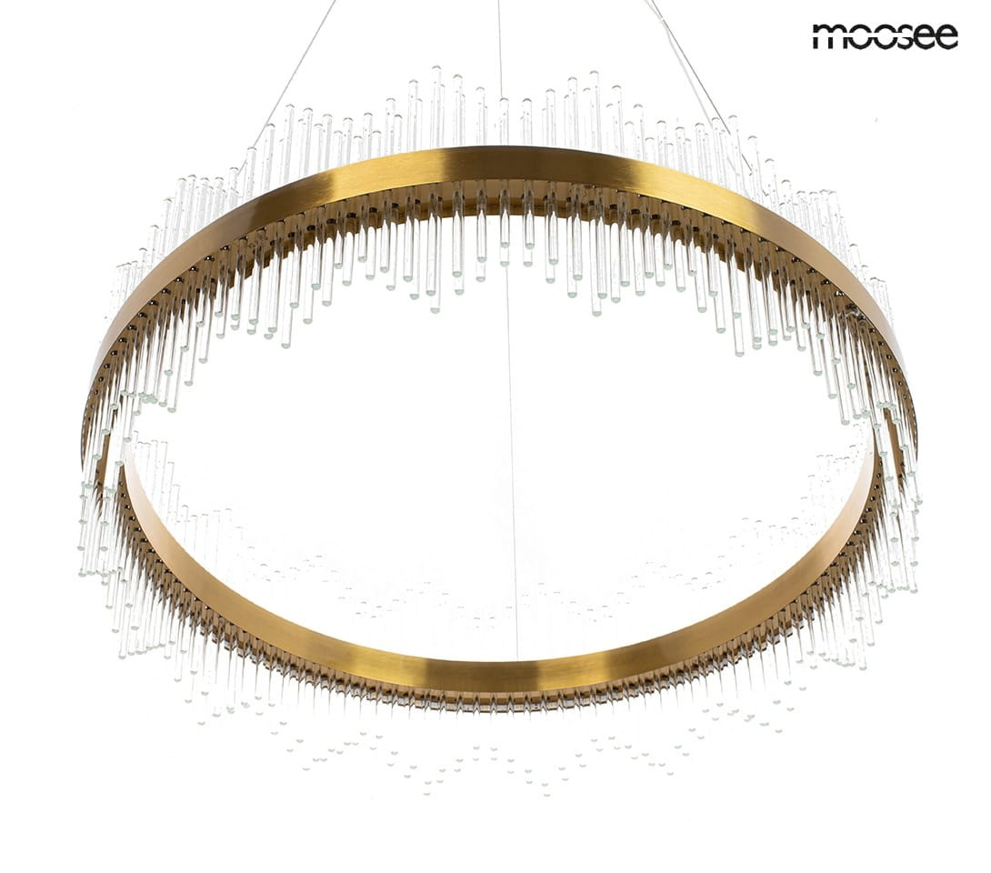 Lampa wisząca Florens 80 LED w złotym kolorze, okrągła konstrukcja z przezroczystymi elementami. Zawieszona na cienkich linkach, z dekoracyjnymi szklanymi prętami, tworzy efektowną iluminację w nowoczesnym wnętrzu.