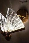 Złoty kinkiet LED Butterfly S z przezroczystym kloszem w kształcie motyla, wykonanym z teksturowanego szkła. Ujęcie z boku, ukazujące detal wzoru klosza oraz montaż na ścianie. Oświetlenie emituje ciepłe światło, tworząc przytulną atmosferę.
