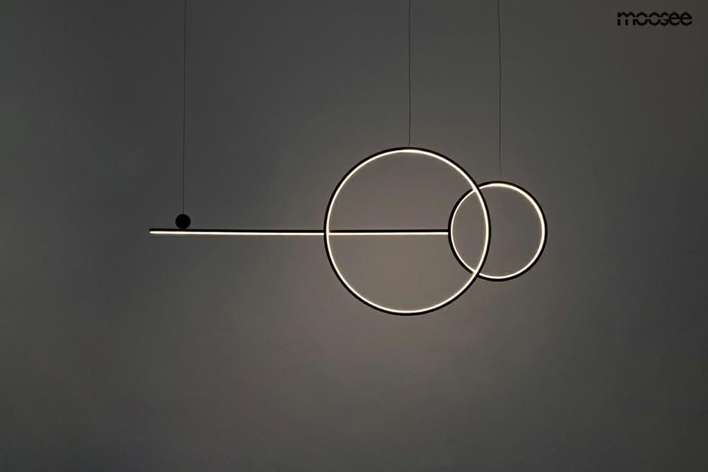 Czarna lampa wisząca Rage LED o trzech punktach świetlnych, z geometrycznymi kształtami: długi poziomy element oraz dwa okręgi, zawieszona na cienkich linkach. Tło jasnoszare, minimalistyczne, podkreślające nowoczesny design.