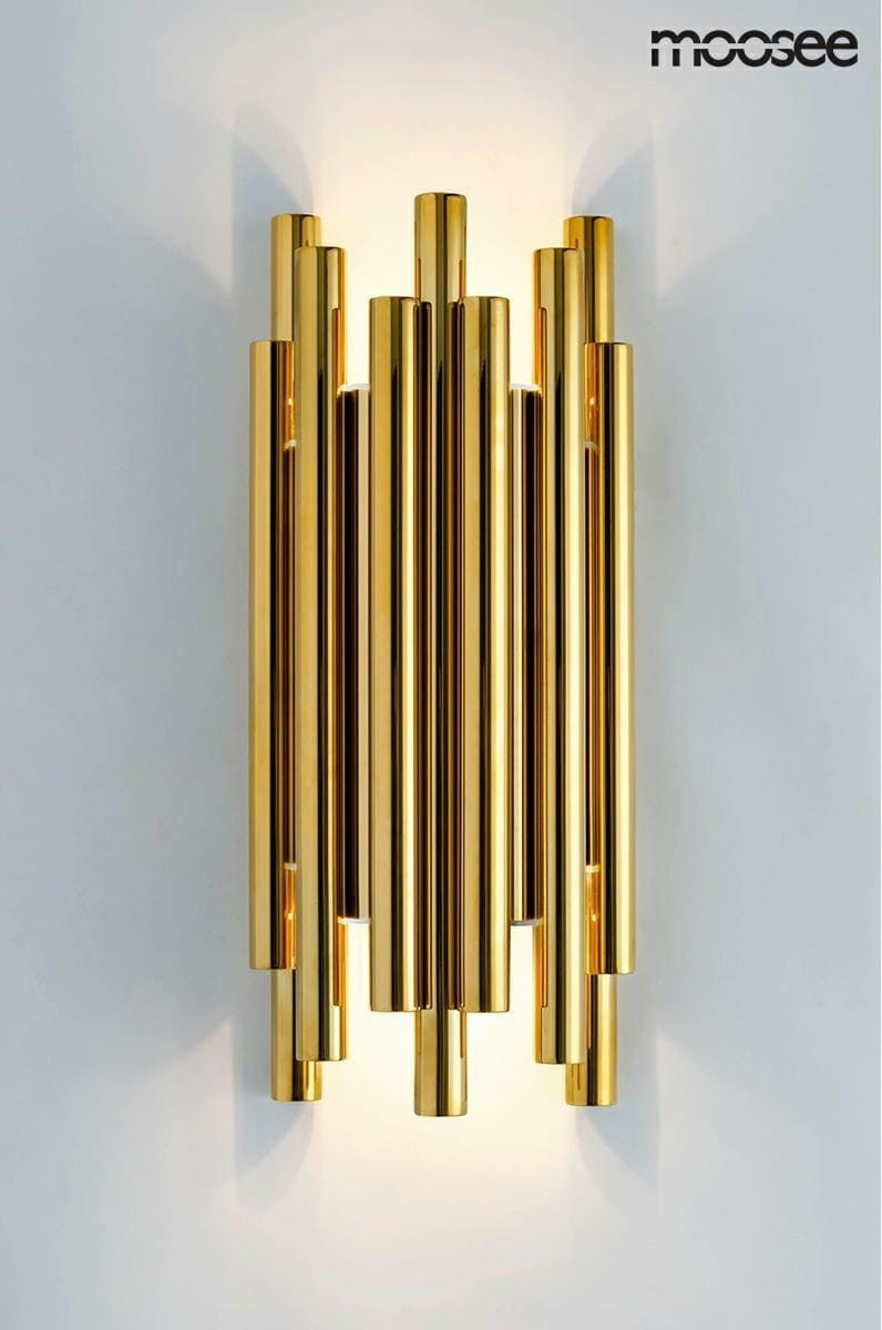 Kinkiet LED Organo w złotym kolorze, składający się z ośmiu cylindrycznych elementów o błyszczącej powierzchni. Produkt zamontowany na ścianie, emitujący światło w górę i w dół, tworząc efektowne oświetlenie. Tło jest jasne i jednolite.