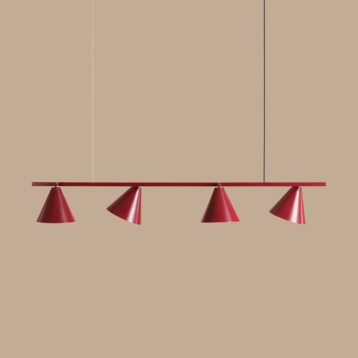Czteropunktowa lampa wisząca Form Red Wine w kolorze czerwonym, złożona z czterech stożkowatych kloszy zawieszonych na prostokątnej listwie. Klosze mają matowe wykończenie, a lampa jest zawieszona na cienkim przewodzie. Tło jasnobeżowe.