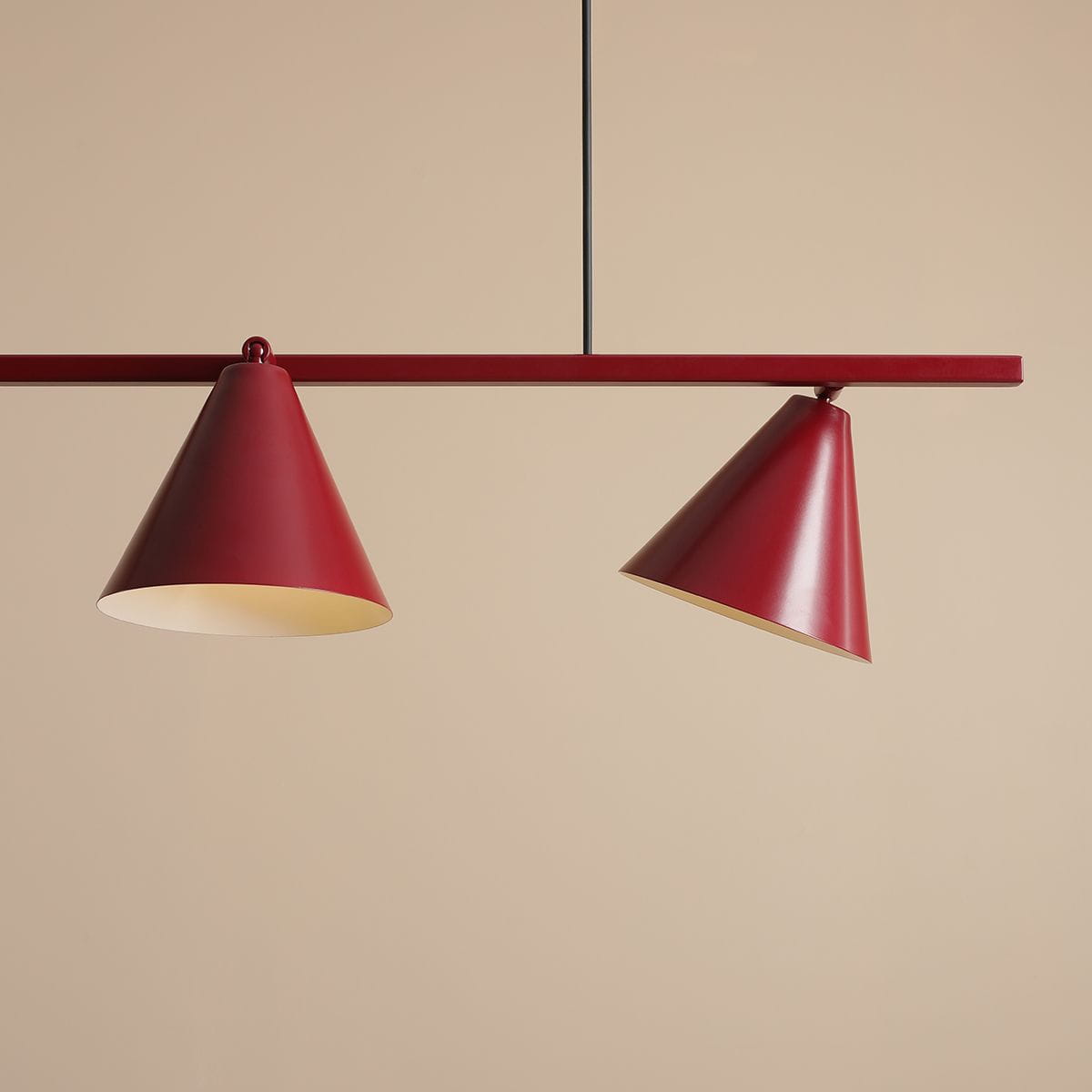 Czteropunktowa lampa wisząca Form Red Wine z czerwonymi kloszami w kształcie stożków, zawieszona na cienkim czarnym przewodzie. Klosze mają jasne wnętrze, a całość umieszczona na gładkim, jasnobrązowym tle.