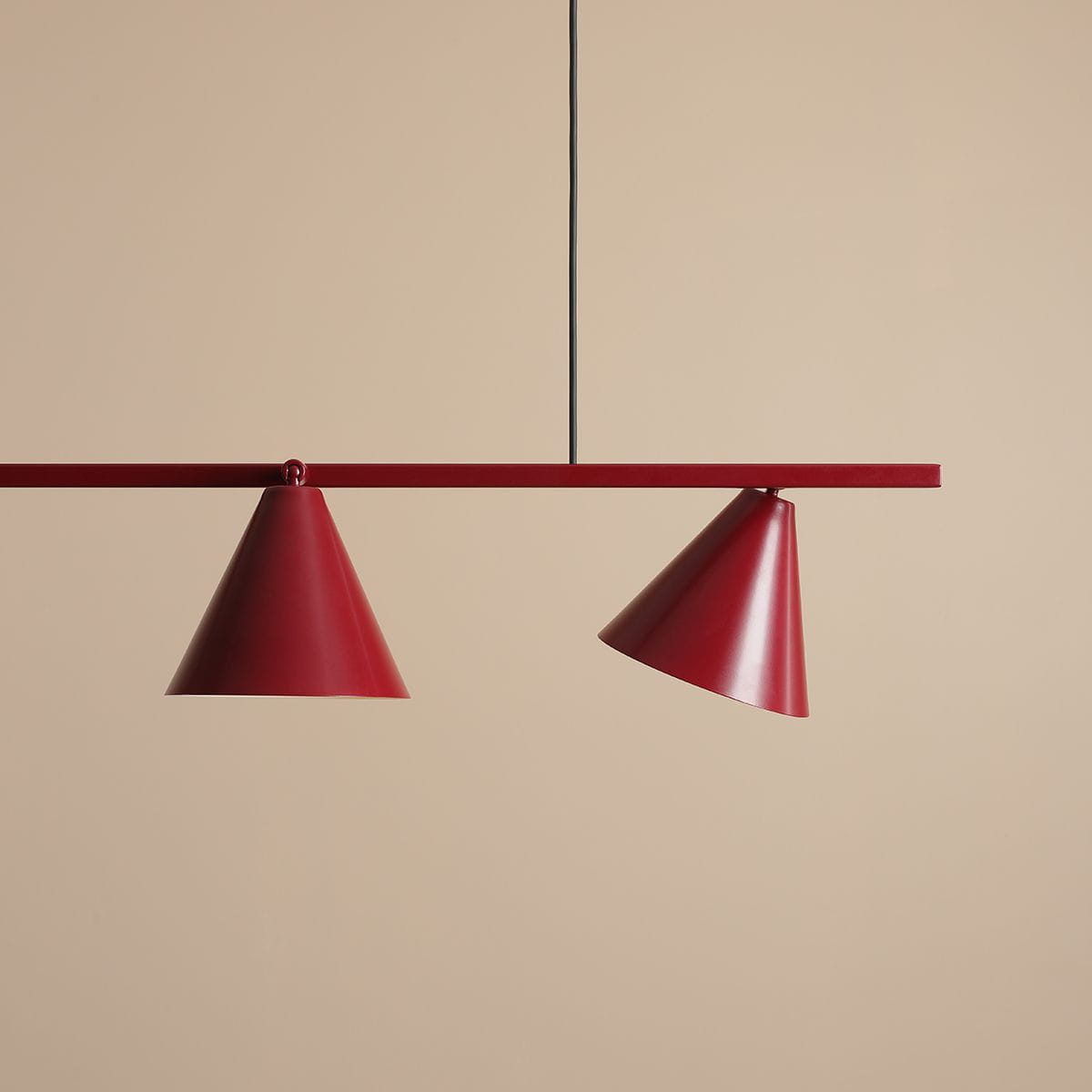 Lampa wisząca Form Red Wine, 4-punktowa, z dwoma stożkowymi kloszami w intensywnym odcieniu czerwieni, zawieszona na prostokątnej metalowej belce. Ujęcie frontalne na tle jasnobeżowej ściany.