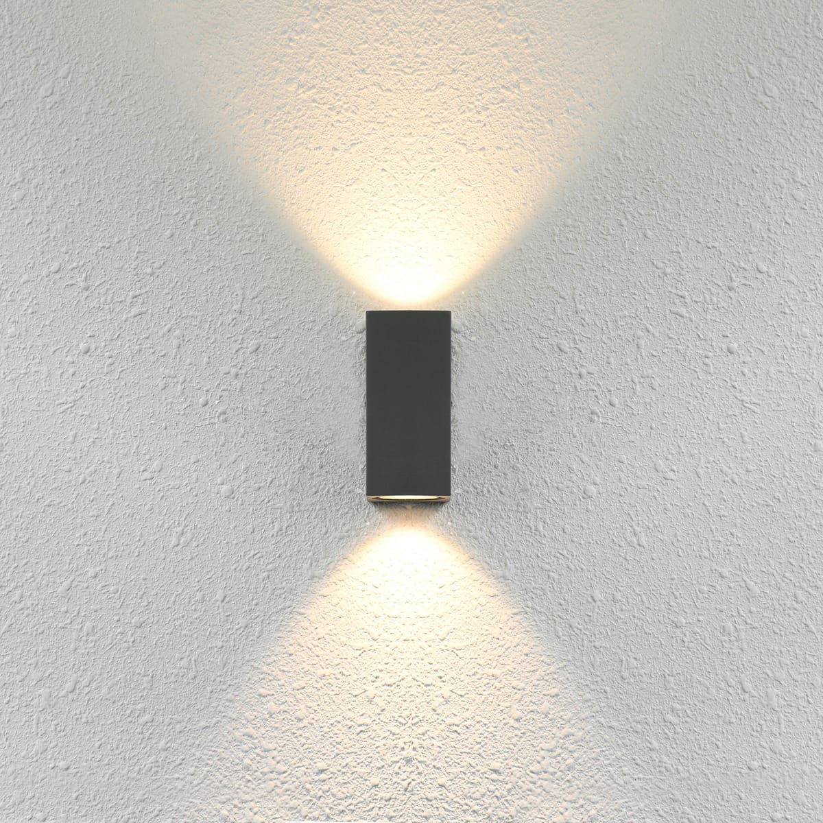 Kinkiet elewacyjny Genta 2-punktowy w kolorze czarnym, zamontowany na białej, teksturowanej ścianie. Emituje światło w górę i w dół, podkreślając fakturę tła. Prosty, prostokątny kształt, minimalistyczny design.