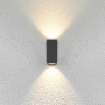 Kinkiet elewacyjny Genta 2-punktowy w kolorze czarnym, zamontowany na białej, teksturowanej ścianie. Emituje światło w górę i w dół, podkreślając fakturę tła. Prosty, prostokątny kształt, minimalistyczny design.