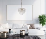 Lampa wisząca Buena 4-punktowa w antycznym brązie, z przezroczystymi kryształkami, zawieszona nad szklanym stołem. W tle białe ściany i roślina, co podkreśla elegancki styl aranżacji wnętrza.