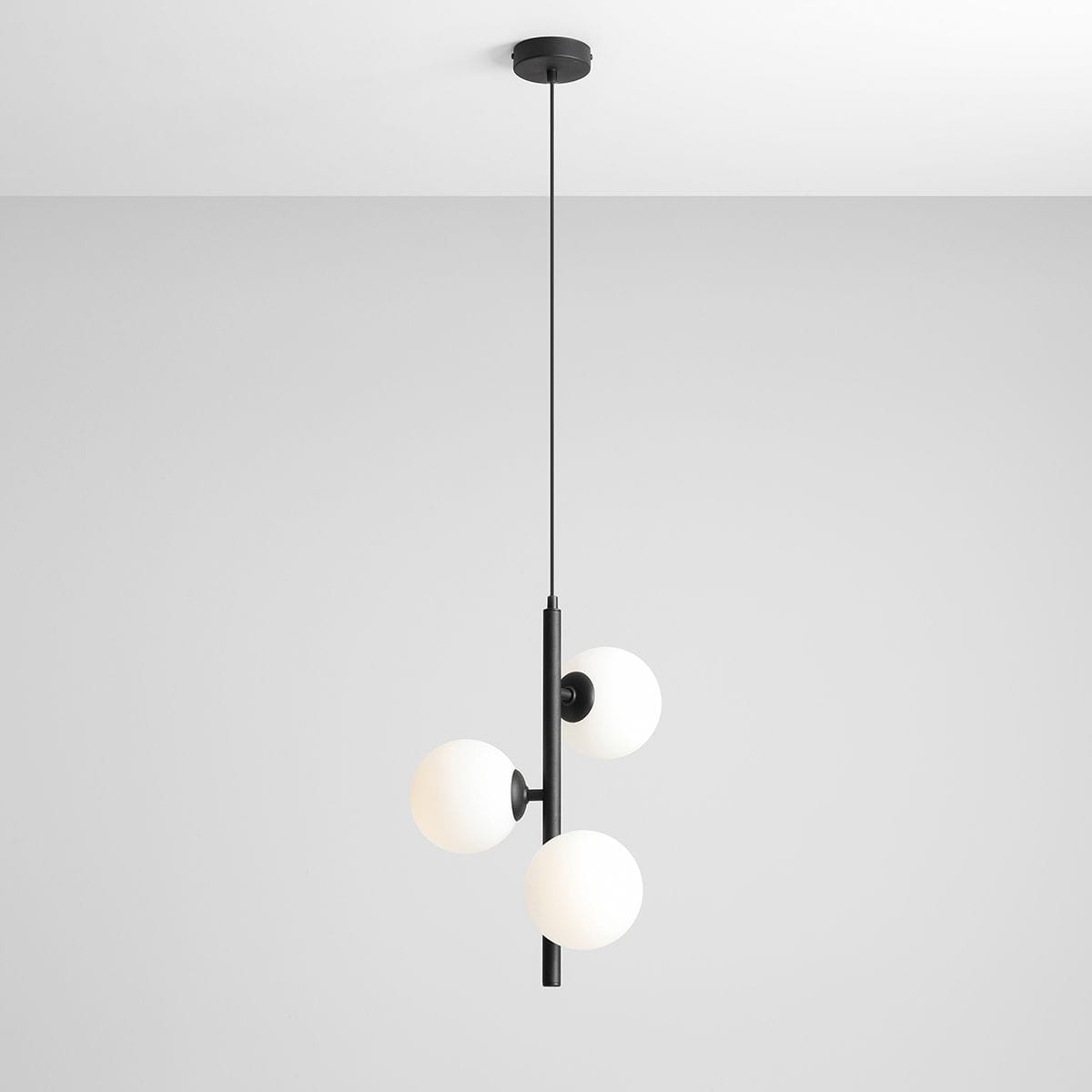 Lampa wisząca Fin S, czarna, z trzema okrągłymi kloszami w białym kolorze. Ujęcie z boku, wisząca na cienkim przewodzie, zamontowana pod sufitem na okrągłej podsufitce. Minimalistyczny design, idealna do nowoczesnych wnętrz.