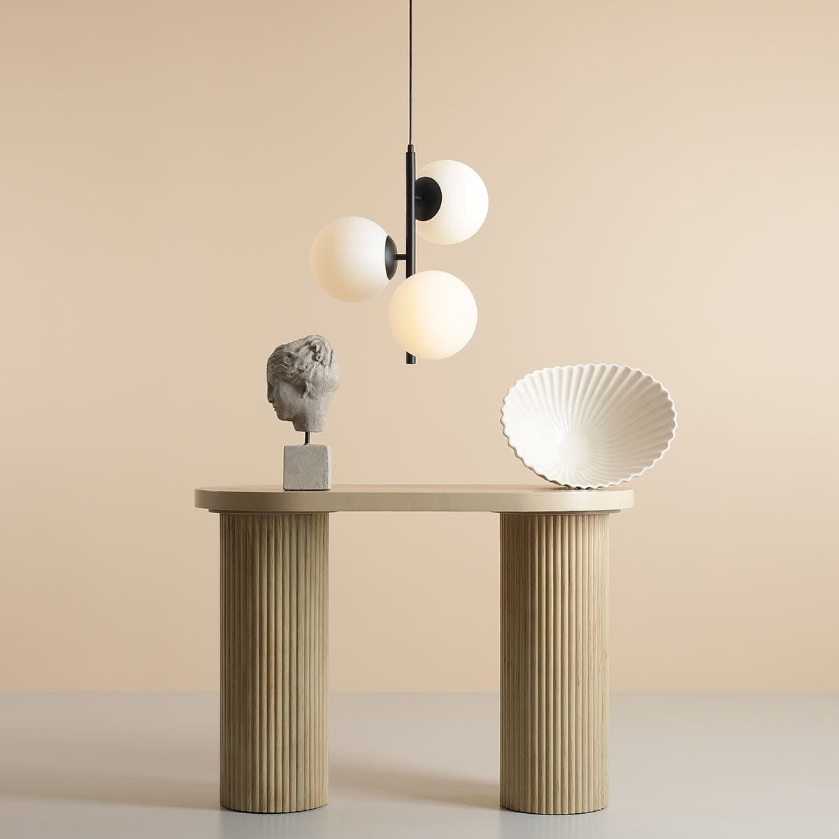 Lampa wisząca Fin M 3-punktowa w kolorze czarnym, z trzema okrągłymi, matowymi kloszami w kolorze białym. Zawieszona nad stołem z kolumnami, w minimalistycznym otoczeniu. Tło w delikatnym odcieniu beżu.