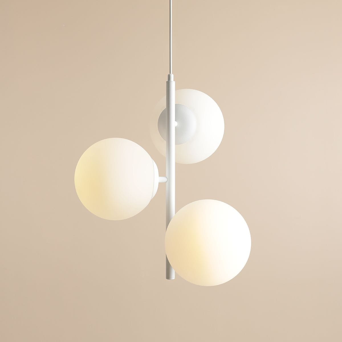 Lampa wisząca Fin M 3-punktowa w kolorze białym, z trzema okrągłymi kloszami z mlecznego szkła, zawieszona na cienkim metalowym stelażu. Klosze rozmieszczone w różnych wysokościach, na tle jasnej ściany.