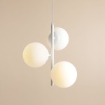 Lampa wisząca Fin M 3-punktowa w kolorze białym, z trzema okrągłymi kloszami z mlecznego szkła, zawieszona na cienkim metalowym stelażu. Klosze rozmieszczone w różnych wysokościach, na tle jasnej ściany.