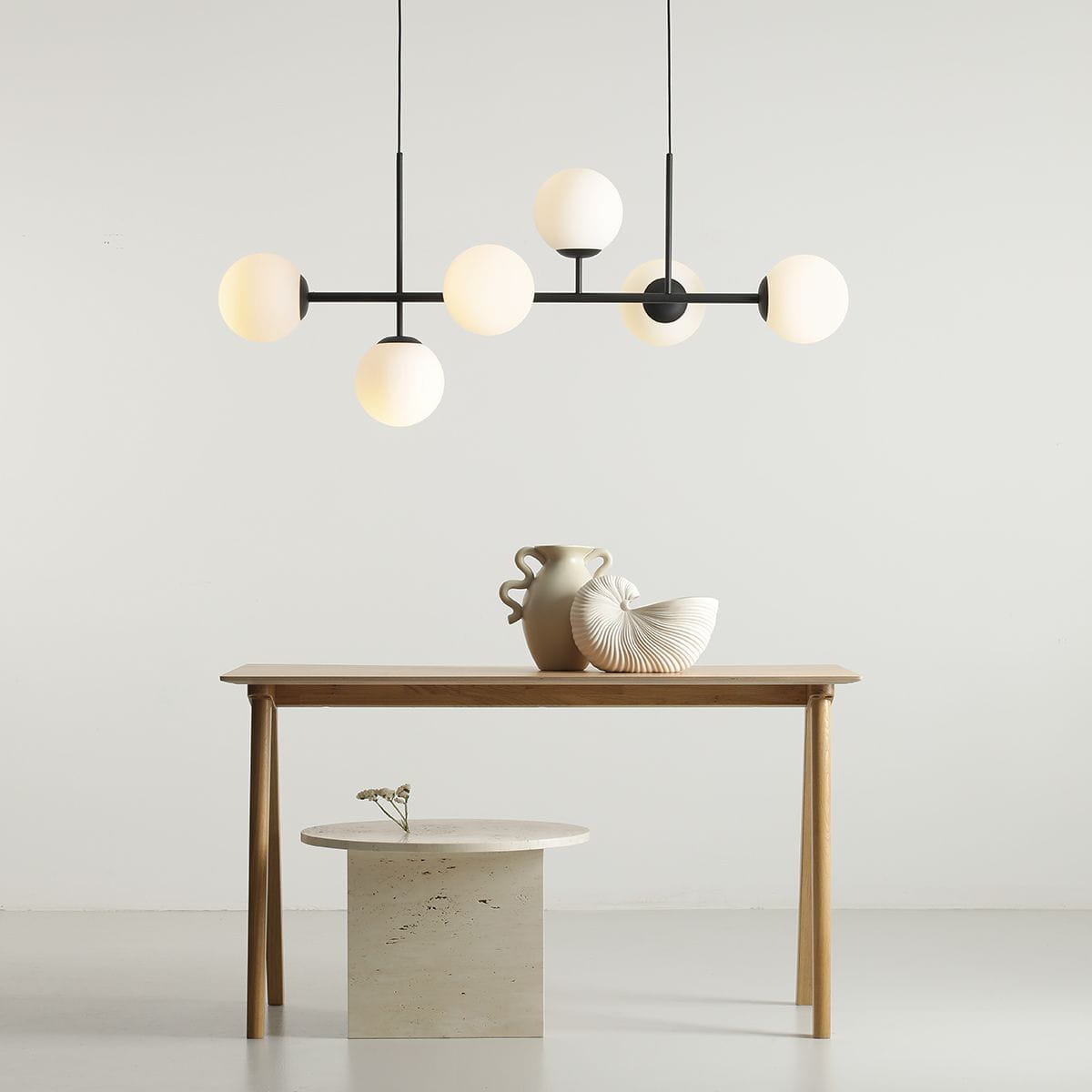 Lampa wisząca Fin 6-punktowa w kolorze czarnym z sześcioma okrągłymi kloszami w odcieniu białym, zawieszona nad drewnianym stołem. W tle widoczne dekoracje: wazon i ceramiczny element dekoracyjny. Proste, jasne tło.