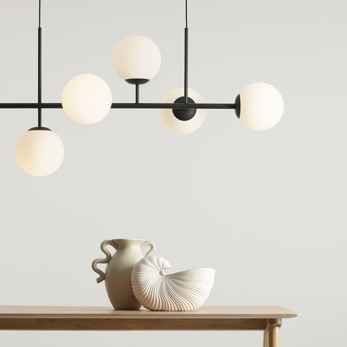 Lampa wisząca Fin 6-punktowa w kolorze czarnym, z sześcioma okrągłymi kloszami w odcieniu białym, zawieszona na cienkich prętach. Widoczne w tle dekoracyjne naczynia na drewnianym stole. Tło jasne, minimalistyczne.