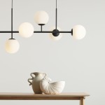 Lampa wisząca Fin 6-punktowa w kolorze czarnym, z sześcioma okrągłymi kloszami w odcieniu białym, zawieszona na cienkich prętach. Widoczne w tle dekoracyjne naczynia na drewnianym stole. Tło jasne, minimalistyczne.
