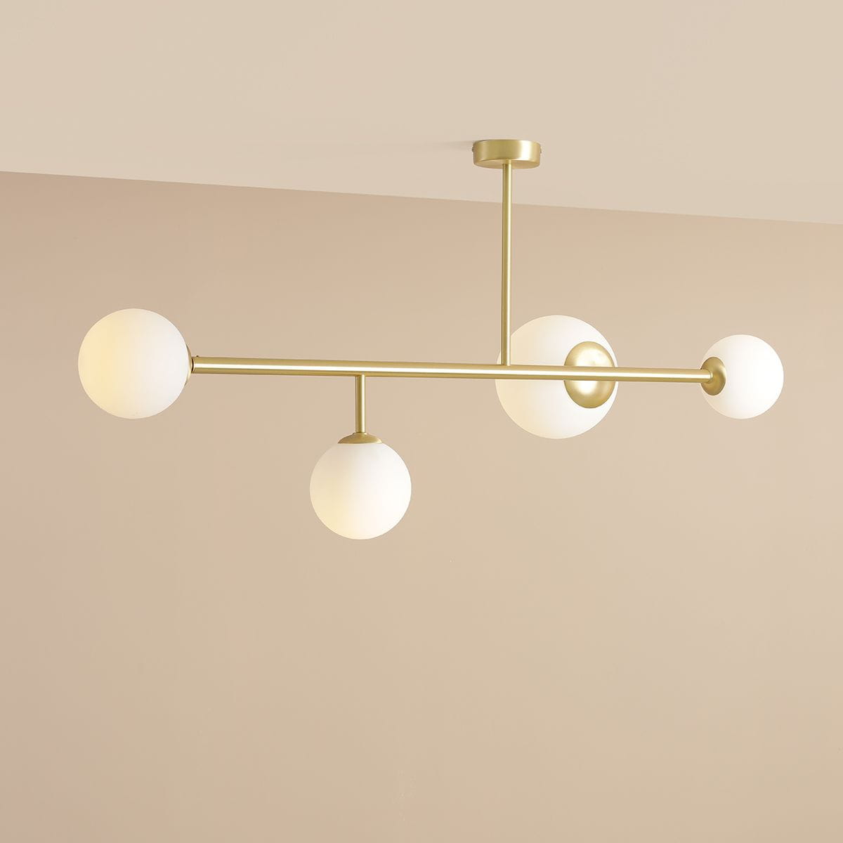 Lampa sufitowa Dione w kolorze mosiądzu z czterema białymi, matowymi kulami. Ujęcie z góry, ukazujące równoległe ramiona. Lampa zamontowana na suficie, dobrze widoczna na jednolitym tle.