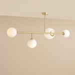 Lampa sufitowa Dione w kolorze mosiądzu z czterema białymi, matowymi kulami. Ujęcie z góry, ukazujące równoległe ramiona. Lampa zamontowana na suficie, dobrze widoczna na jednolitym tle.