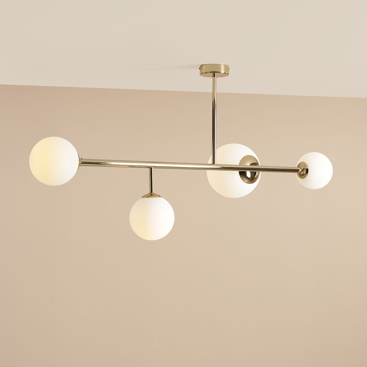 Lampa sufitowa Dione 4-punktowa w kolorze złotym. Konstrukcja z metalowych prętów z czterema okrągłymi kloszami z mlecznego szkła. Ujęcie z góry, wisząca, na jasnym tle, z eleganckim wykończeniem.