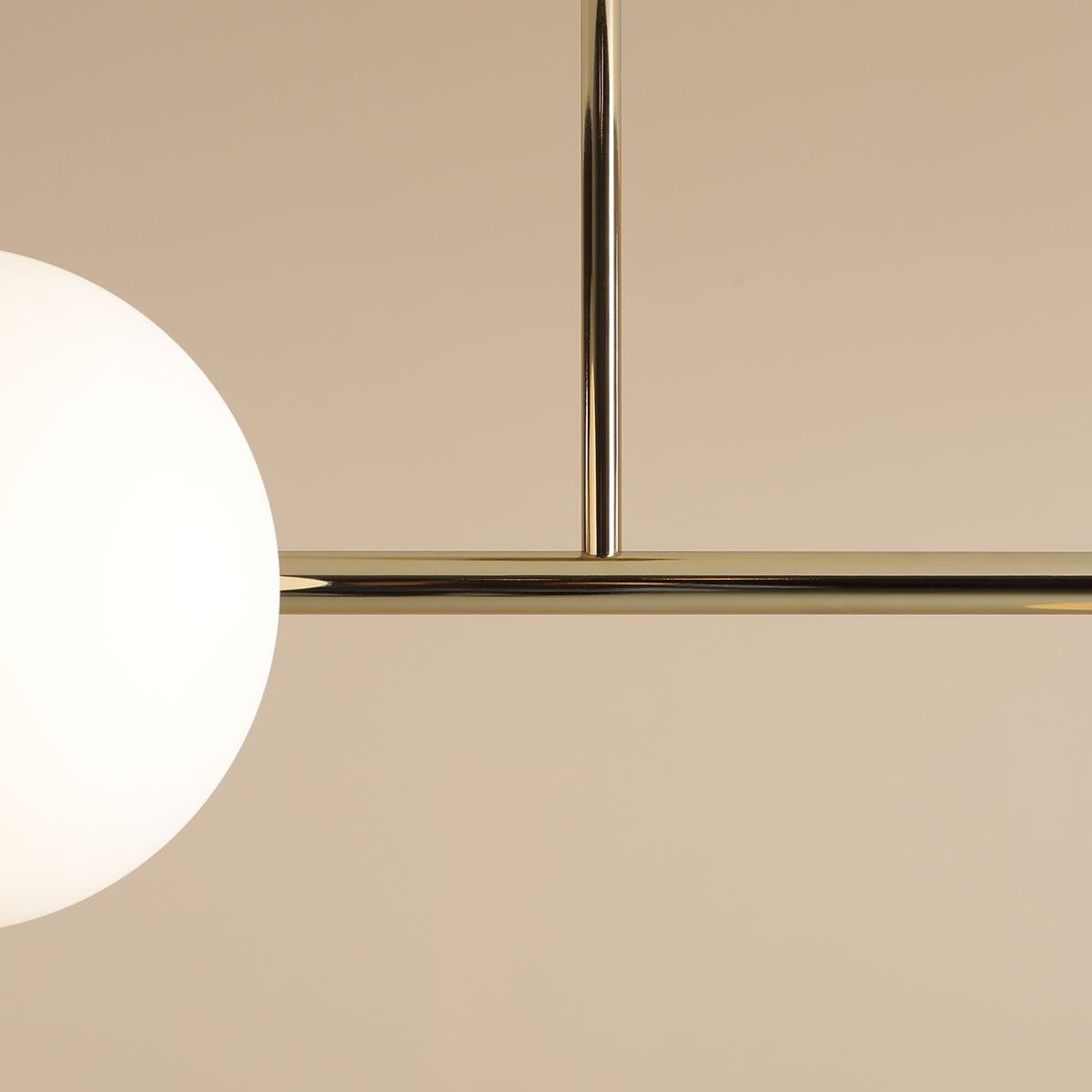 Złota lampa sufitowa Dione z czterema punktami świetlnymi. Konstrukcja metalowa, z białymi kulistymi kloszami, zawieszona na poziomej belce. Ujęcie z bliska, ukazujące detale wykończenia i kształt kloszy. Tło w delikatnym beżu.